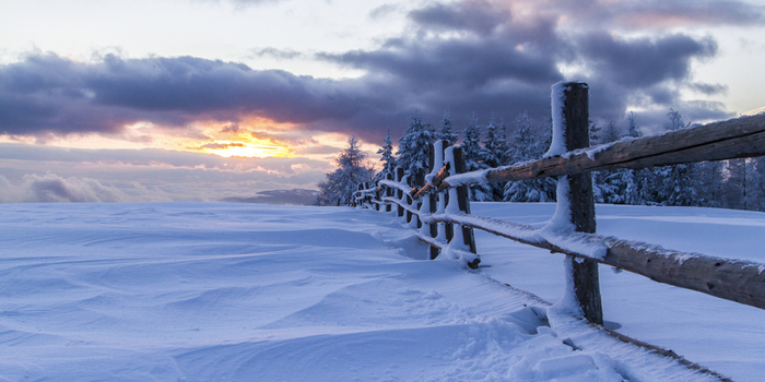 View of a snow laden wooden fence cutting across a vast expanse of white the sky ablaze with the fiery hues of sunset Schöckl Styria Austria. View of a snow laden wooden fence cutting across a vast expanse of white the sky ablaze with the fiery hues of sunset Schöckl Styria Austria.
