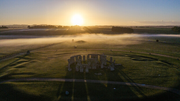 Aerial view of Stonehenge surrounded by mist in the green fields at sunrise in Salisbury England United Kingdom. Aerial view of Stonehenge surrounded by mist in the green fields at sunrise in Salisbury England United Kingdom.