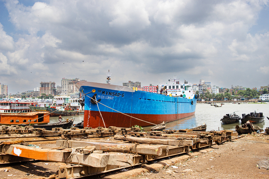 Keraniganj Bangladesh 04 September 2024 View of the Shipyard Dhaka featuring a large blue cargo ship docked near wooden beams with the city skyline under a cloudy sky.