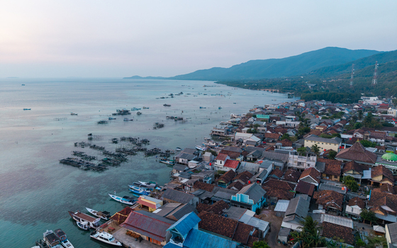 Aerial view of Karimunjawa village with traditional houses fishing boats in shallow turquoise waters and lush mountains in the background in Karimunjawa Central Java Indonesia. Aerial view of Karimunjawa village with traditional houses fishing boats in shallow turquoise waters and lush mountains in the background in Karimunjawa Central Java Indonesia.