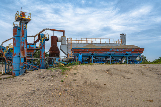 View of industrial stone processing machinery with blue metal structures and a worker in blue overalls standing near a gravel hopper at the Lamingo quarry site in Jos Plateau Nigeria.