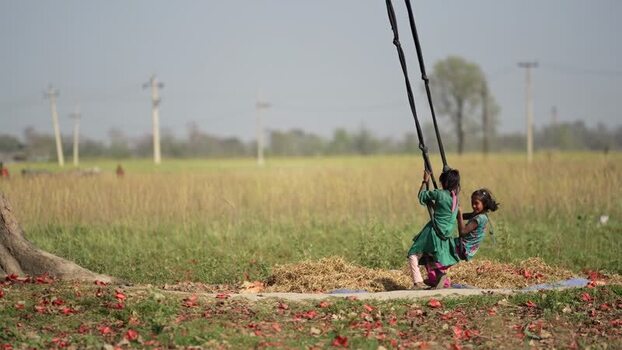 View of two girls playing on a swing in a rural field Nepal.