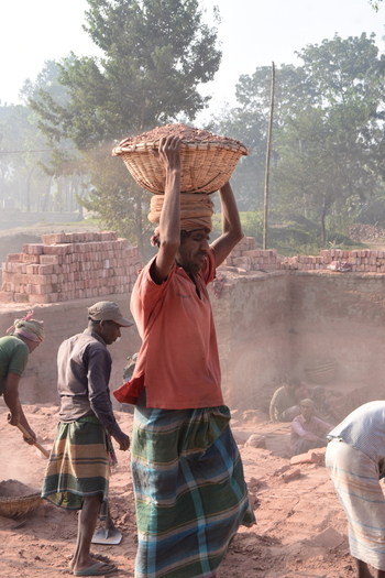 Kushtia District Khulna Division Bangladesh 28 November 2020 View of a worker carrying a basket of bricks on his head at a brick factory with other laborers working in the dusty outdoor site. Kushtia District Khulna Division Bangladesh 28 November 2020 View of a worker carrying a basket of bricks on his head at a brick factory with other laborers working in the dusty outdoor site.