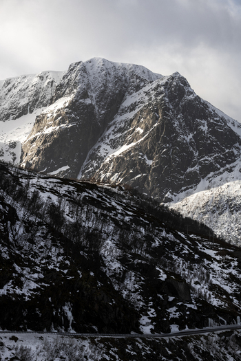 View of rugged snow covered mountain peaks and rocky cliffs above a winding road Kvaloya Troms Norway. View of rugged snow covered mountain peaks and rocky cliffs above a winding road Kvaloya Troms Norway.
