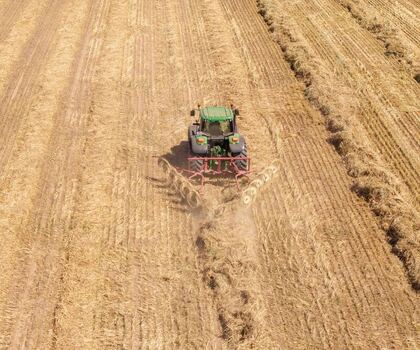 Aerial view of a green tractor pulling a hay rake through a dry harvested field in Philadelphia Western Cape South Africa. Aerial view of a green tractor pulling a hay rake through a dry harvested field in Philadelphia Western Cape South Africa.