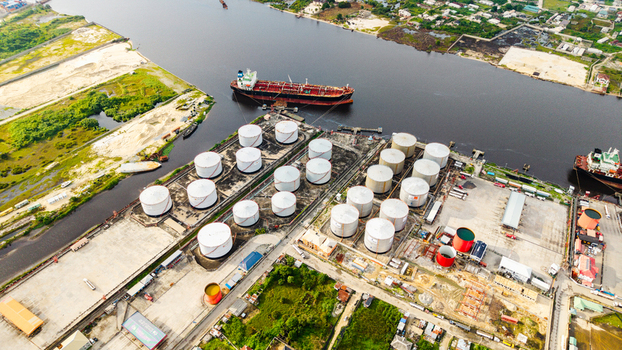 Aerial view of the Satellite Town oil storage facility featuring numerous large white cylindrical tanks industrial infrastructure and a tanker ship docked in the river in Lagos Lagos Nigeria.