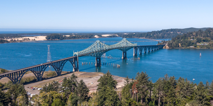 Aerial view of the McCullough Memorial Bridge spanning the Coos Bay surrounded by lush evergreen forests and blue water in North Bend Oregon United States. Aerial view of the McCullough Memorial Bridge spanning the Coos Bay surrounded by lush evergreen forests and blue water in North Bend Oregon United States.
