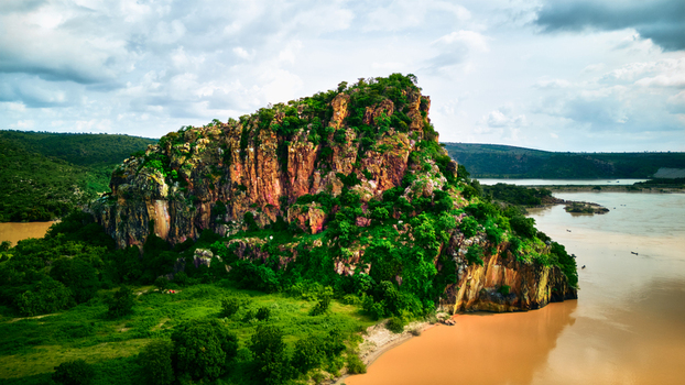 Aerial view of the rocky Jebba formation rising above the Niger River surrounded by lush green vegetation under a cloudy sky in Jebba Niger Nigeria.