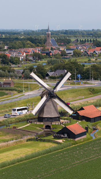 Aerial view of the historic windmill surrounded by green fields a small village and a road with a bus under a clear sky in Schermerhorn North Holland Netherlands. Aerial view of the historic windmill surrounded by green fields a small village and a road with a bus under a clear sky in Schermerhorn North Holland Netherlands.