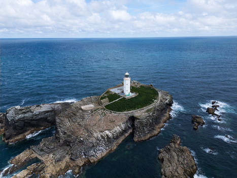 Aerial view of Godrevy Lighthouse situated on a rocky island surrounded by the blue waters of the Atlantic Ocean under a cloudy sky in Gwithian England United Kingdom. Aerial view of Godrevy Lighthouse situated on a rocky island surrounded by the blue waters of the Atlantic Ocean under a cloudy sky in Gwithian England United Kingdom.