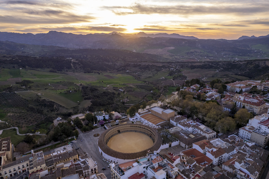 Aerial view of the historic Plaza de Toros de Ronda bullring surrounded by traditional white buildings and rolling mountains at sunset in Ronda Andalusia Spain. Aerial view of the historic Plaza de Toros de Ronda bullring surrounded by traditional white buildings and rolling mountains at sunset in Ronda Andalusia Spain.