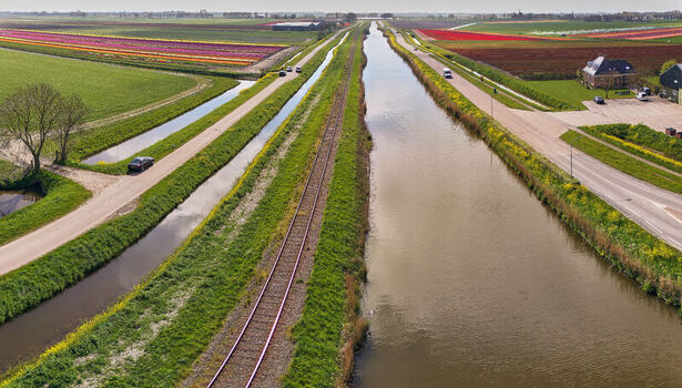 Aerial view of colorful tulip fields railway tracks of the Hoorn Medemblik steam train and a canal under a clear sky Abbekerk North Holland Netherlands. Aerial view of colorful tulip fields railway tracks of the Hoorn Medemblik steam train and a canal under a clear sky Abbekerk North Holland Netherlands.