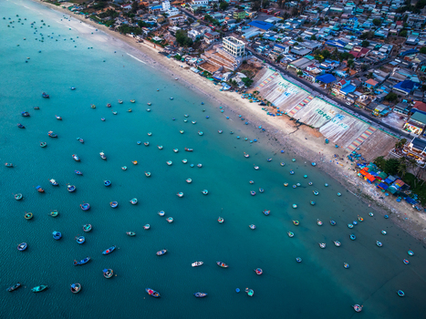 Aerial view of traditional round basket boats floating in the turquoise waters off the coast of Mui Ne with a sandy beach and coastal town infrastructure in Vietnam. Aerial view of traditional round basket boats floating in the turquoise waters off the coast of Mui Ne with a sandy beach and coastal town infrastructure in Vietnam.