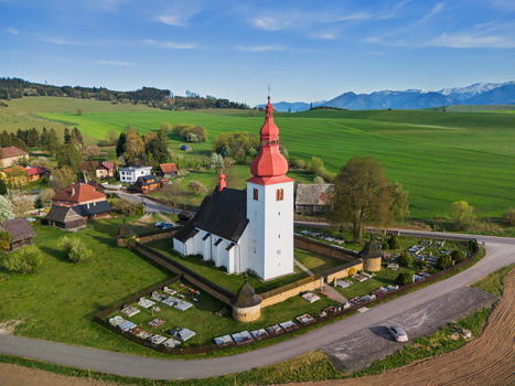 Aerial view of the Church of Saint Ladislaus with its red onion dome and stone wall surrounded by green fields and mountains in Liptovske Matiasovce Zilina Region Slovakia.