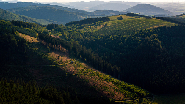 Aerial view of the rolling hills and dense coniferous forests of the Sauerland region featuring sunlit slopes and shadows in Eslohe North Rhine Westphalia Germany. Aerial view of the rolling hills and dense coniferous forests of the Sauerland region featuring sunlit slopes and shadows in Eslohe North Rhine Westphalia Germany.