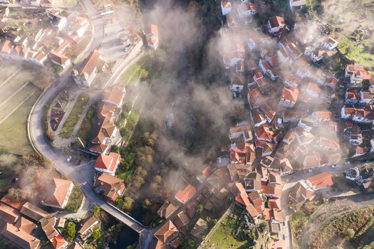 Aerial view of Avo village with red tiled roofs and mist rising from the river valley in Oliveira do Hospital Coimbra District Portugal.