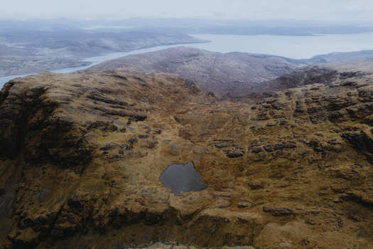 Aerial view of the rocky slopes and summit of Bla Bheinn featuring a small dark mountain tarn nestled in the rugged landscape of the Isle of Skye Scotland United Kingdom. Aerial view of the rocky slopes and summit of Bla Bheinn featuring a small dark mountain tarn nestled in the rugged landscape of the Isle of Skye Scotland United Kingdom.