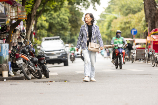 Hanoi Ha Noi Vietnam 11 November 2025 View of an elderly woman walking along a busy street with motorbikes and parked vehicles in the background.