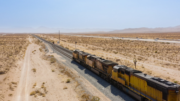 Aerial view of a freight train traveling through the vast desert landscape with a highway in the background in the United States.