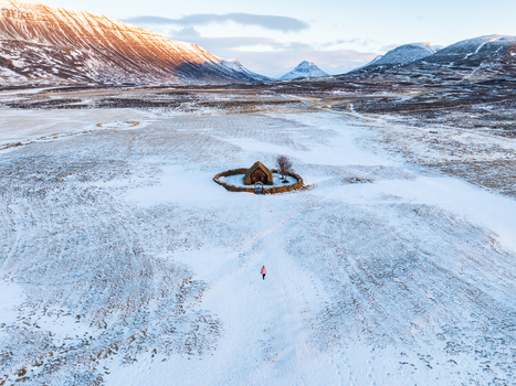 Aerial view of Grafarkirkja a historic turf church surrounded by a stone wall in a snowy landscape with a person walking towards it under golden hour light in Hofsos Skagafjordur Iceland. Aerial view of Grafarkirkja a historic turf church surrounded by a stone wall in a snowy landscape with a person walking towards it under golden hour light in Hofsos Skagafjordur Iceland.