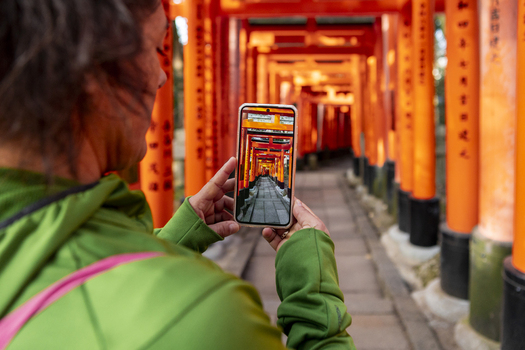 View of a woman taking a photo with her smartphone of the vermilion Senbon Torii gates at Fushimi Inari taisha shrine in Kyoto Kyoto Japan.