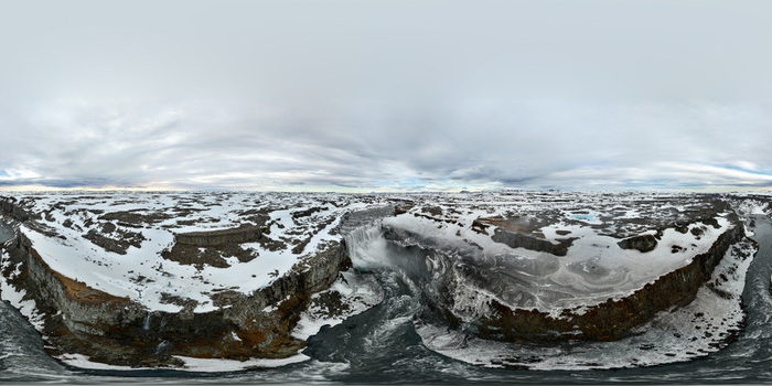 Aerial view of Dettifoss waterfall cascading into a deep canyon surrounded by snow covered rocky cliffs under a cloudy sky Nordurthing Iceland.