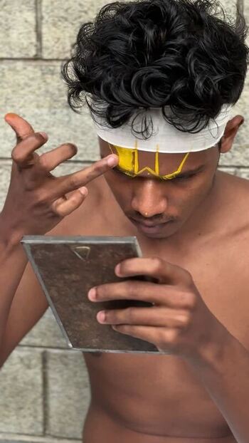 View of a young man applying traditional yellow face paint in Kochi India. View of a young man applying traditional yellow face paint in Kochi India.