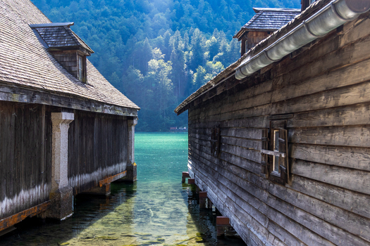 View of traditional wooden boathouses on the turquoise water of Konigssee with dense forest in the background in Schonau am Konigssee Bavaria Germany.