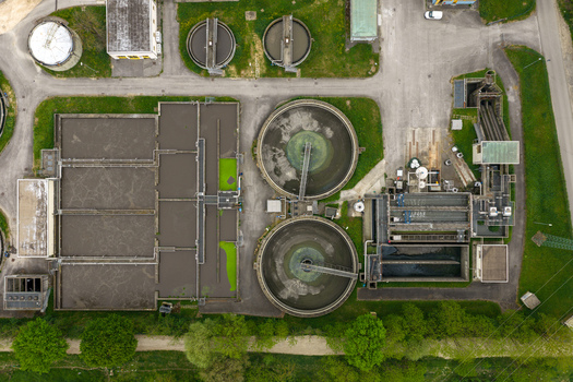 Aerial view of a wastewater treatment plant featuring circular clarifiers and rectangular aeration tanks surrounded by green grass in San Giovanni Valdarno Tuscany Italy.