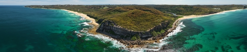 Aerial view of deep turquoise waves crashing against the rugged coastline and sandy beaches contrasting with the lush green headland Newcastle New South Wales Australia.