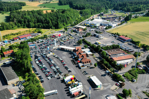 Aerial view of the Eventzentrum Strohofer Geiselwind musichall with large parking lots trucks and a gas station surrounded by green forests in Geiselwind Bayern Germany. Aerial view of the Eventzentrum Strohofer Geiselwind musichall with large parking lots trucks and a gas station surrounded by green forests in Geiselwind Bayern Germany.