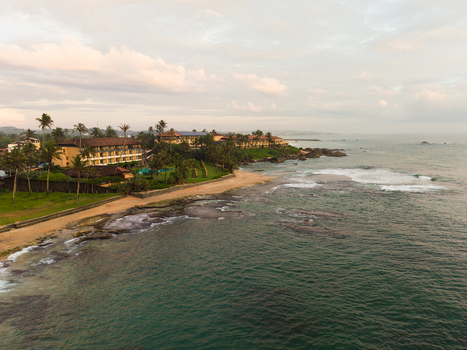 Aerial view of Gintota beach featuring a coastal resort nestled among palm trees along the rocky shoreline under a soft sunset sky in Galle Southern Province Sri Lanka. Aerial view of Gintota beach featuring a coastal resort nestled among palm trees along the rocky shoreline under a soft sunset sky in Galle Southern Province Sri Lanka.