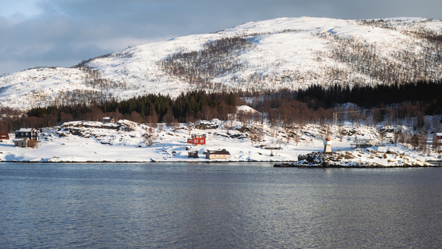 View of a serene landscape where the tranquil waters meet snow covered shores with scattered houses nestled against a backdrop of snow capped mountains Brensholmen Troms Norway. View of a serene landscape where the tranquil waters meet snow covered shores with scattered houses nestled against a backdrop of snow capped mountains Brensholmen Troms Norway.