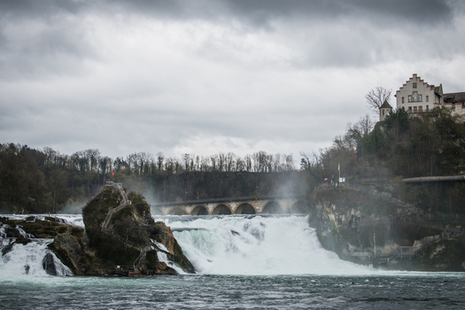 View of cascading waterfalls plunging into the river below with a medieval castle perched on the hill above Schaffhausen Neuhausen am Rheinfall Switzerland. View of cascading waterfalls plunging into the river below with a medieval castle perched on the hill above Schaffhausen Neuhausen am Rheinfall Switzerland.