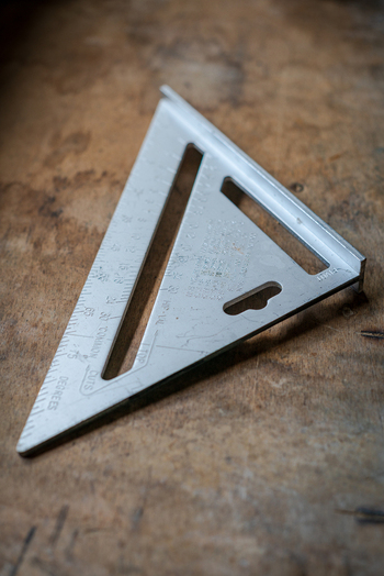 View of a metal speed square resting on a rustic wooden workbench in Looe Cornwall United Kingdom. View of a metal speed square resting on a rustic wooden workbench in Looe Cornwall United Kingdom.