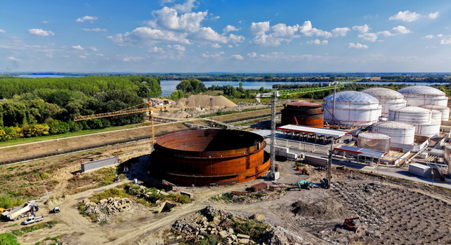 Aerial view of the construction site of an oil storage tank with a large circular steel structure cranes and existing white storage tanks near a river in Kovin Vojvodina Serbia. Aerial view of the construction site of an oil storage tank with a large circular steel structure cranes and existing white storage tanks near a river in Kovin Vojvodina Serbia.