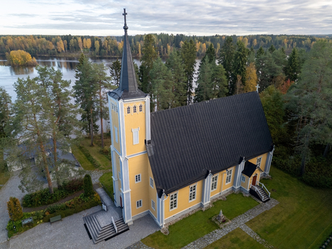 Aerial view of the historic yellow wooden Muhos Church with a black roof and steeple surrounded by autumn trees near the Oulujoki river in Muhos North Ostrobothnia Finland. Aerial view of the historic yellow wooden Muhos Church with a black roof and steeple surrounded by autumn trees near the Oulujoki river in Muhos North Ostrobothnia Finland.
