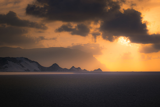 View of Detwah Lagoon with white sand dunes and rugged mountains under a dramatic sunset sky with golden light in Qalansiyah wa Abd Al Kuri Socotra Yemen. View of Detwah Lagoon with white sand dunes and rugged mountains under a dramatic sunset sky with golden light in Qalansiyah wa Abd Al Kuri Socotra Yemen.