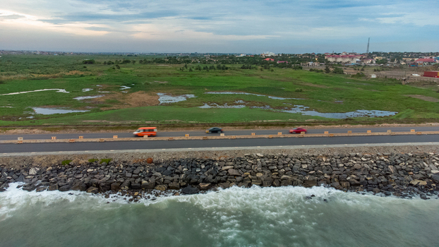 Aerial view of the Accra Tema Beach Road with vehicles driving along the rocky coastline and green wetlands in Accra Greater Accra Region Ghana.