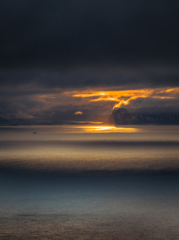 Aerial view of the vast tranquil sea reflecting the fiery glow of the setting sun through a gap in the heavy dark clouds Henningsv&aelig;r Nordland Norway.