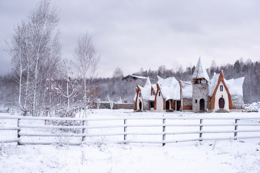 View of the fairy tale Clay Castle of the Valley of Fairies surrounded by a snow covered landscape with a wooden fence in the foreground in Curtea de Arges Judetul Arges Romania. View of the fairy tale Clay Castle of the Valley of Fairies surrounded by a snow covered landscape with a wooden fence in the foreground in Curtea de Arges Judetul Arges Romania.