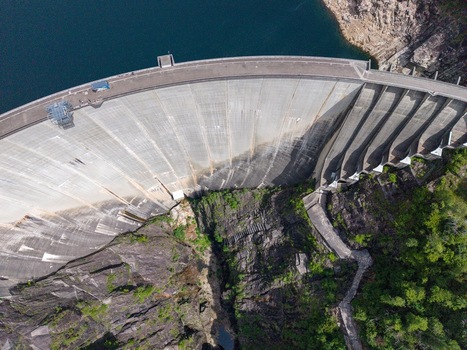 Aerial view of the massive concrete arch of the Verzasca Dam nestled between steep rocky cliffs and lush greenery in Gordola Ticino Switzerland. Aerial view of the massive concrete arch of the Verzasca Dam nestled between steep rocky cliffs and lush greenery in Gordola Ticino Switzerland.