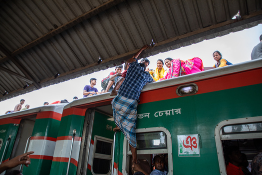 Dhaka Bangladesh 14 June 2018 View of people climbing onto the roof of a crowded train at the Airport Railway Station under a corrugated metal roof. Dhaka Bangladesh 14 June 2018 View of people climbing onto the roof of a crowded train at the Airport Railway Station under a corrugated metal roof.