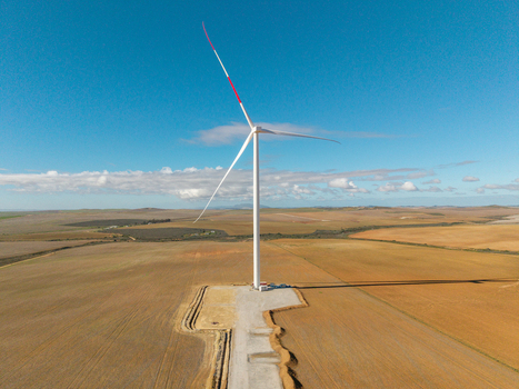 Aerial view of a large wind turbine with red tipped blades standing in a vast agricultural field under a clear blue sky Swellendam Western Cape South Africa. Aerial view of a large wind turbine with red tipped blades standing in a vast agricultural field under a clear blue sky Swellendam Western Cape South Africa.
