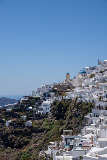 View of white buildings and a blue domed church on the volcanic cliffs under a clear blue sky in Fira Greece. View of white buildings and a blue domed church on the volcanic cliffs under a clear blue sky in Fira Greece.