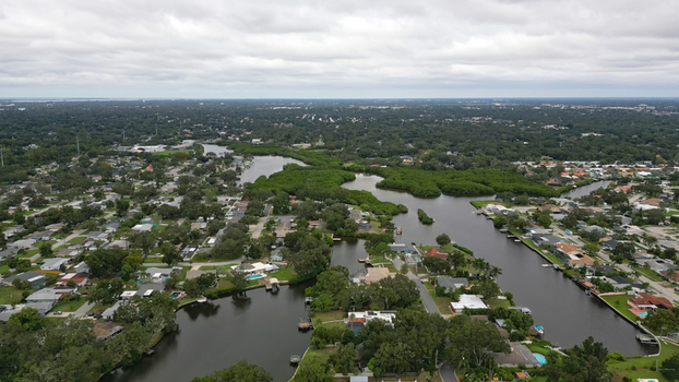 Aerial view of a residential neighborhood featuring winding canals lush green trees and suburban houses under a cloudy sky in Clearwater Florida United States.