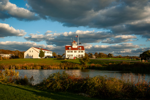 View of the historic Coast Guard Station on Martha s Vineyard with white buildings and red roofs under a dramatic cloudy sky in Edgartown Massachusetts United States.