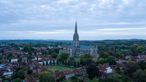 Aerial view of Salisbury Cathedral surrounded by historic rooftops lush green trees and the urban landscape of the city in Salisbury Wiltshire United Kingdom. Aerial view of Salisbury Cathedral surrounded by historic rooftops lush green trees and the urban landscape of the city in Salisbury Wiltshire United Kingdom.