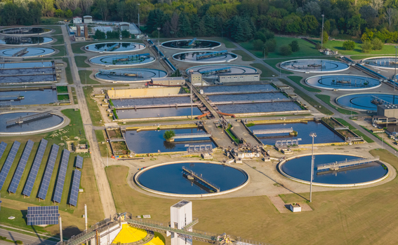 Aerial view of a large wastewater treatment facility featuring circular clarifiers aeration basins and solar panels surrounded by greenery in Italy. Aerial view of a large wastewater treatment facility featuring circular clarifiers aeration basins and solar panels surrounded by greenery in Italy.