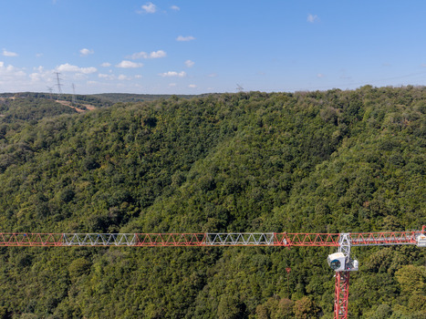 Aerial view of a red and white construction crane jib extending over a dense green forest under a clear blue sky in Istanbul Istanbul Turkiye. Aerial view of a red and white construction crane jib extending over a dense green forest under a clear blue sky in Istanbul Istanbul Turkiye.